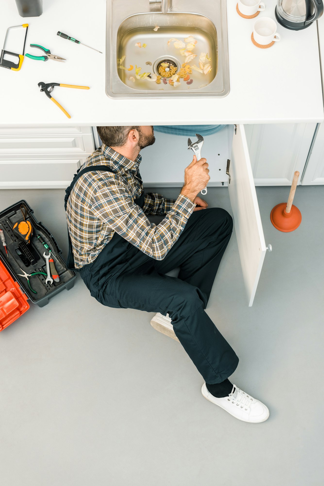 high angle view of plumber repairing sink with adjustable wrench in kitchen